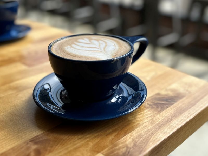 Blue coffee cup on a table with coffee and some creme in it. 