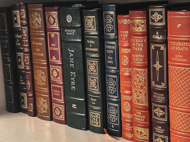 A view of some leatherbound books on a white bookshelf.